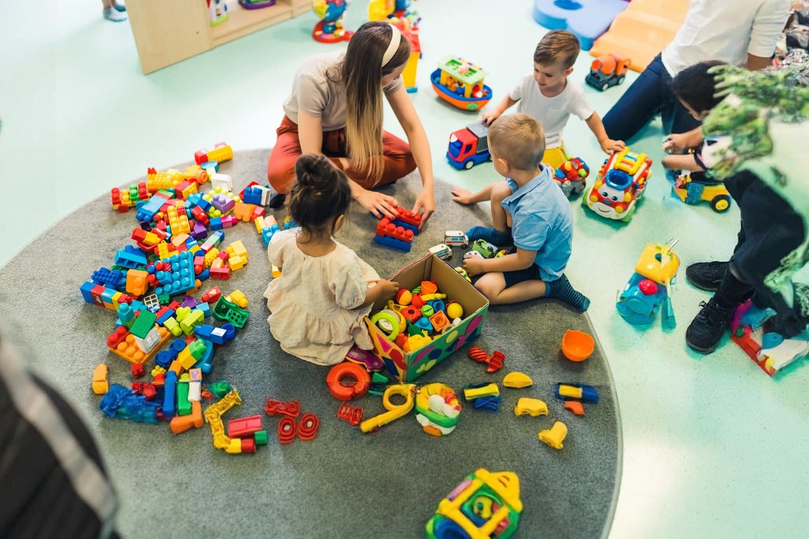 A teacher sitting on the classroom floor building with blocks alongside a group of young children